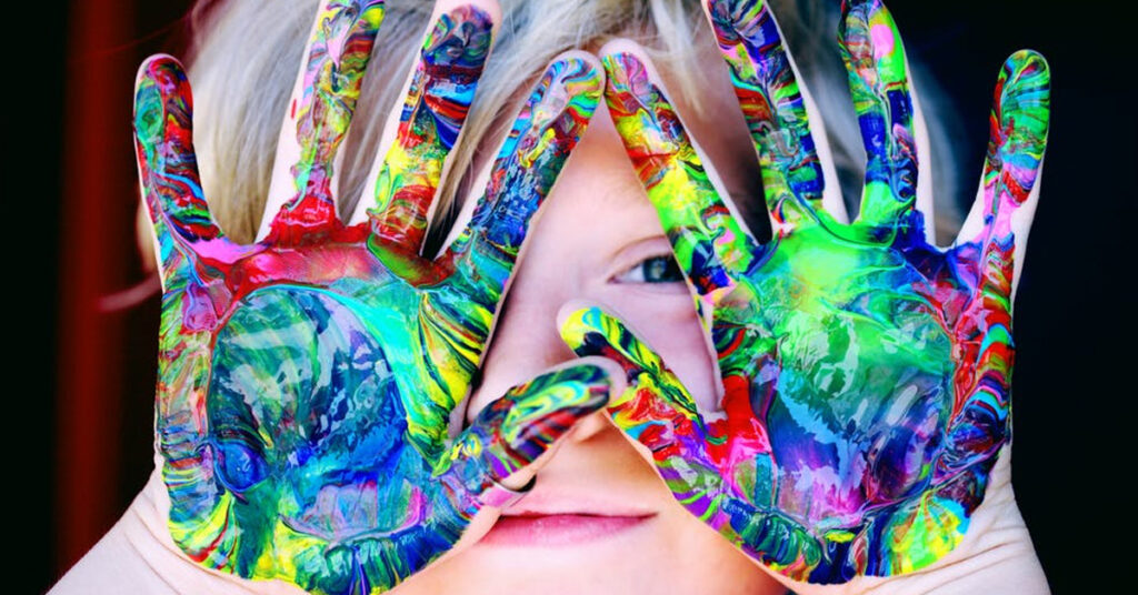Child holding up hands with swirled paint very colorful